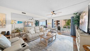 Ein geräumiges Wohnzimmer mit einem beigefarbenen Sofa, einem Holztisch und einem Deckenventilator.