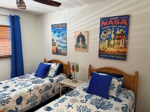 A bedroom with two beds, a nightstand, a lamp, and three posters on the wall. - Wake to Waves, Watch Rockets Soar: Your Dreamy Oceanfront Condo Awaits (Cocoa Beach)