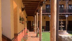 A covered outdoor area with a tiled floor, wooden columns, and potted plants.