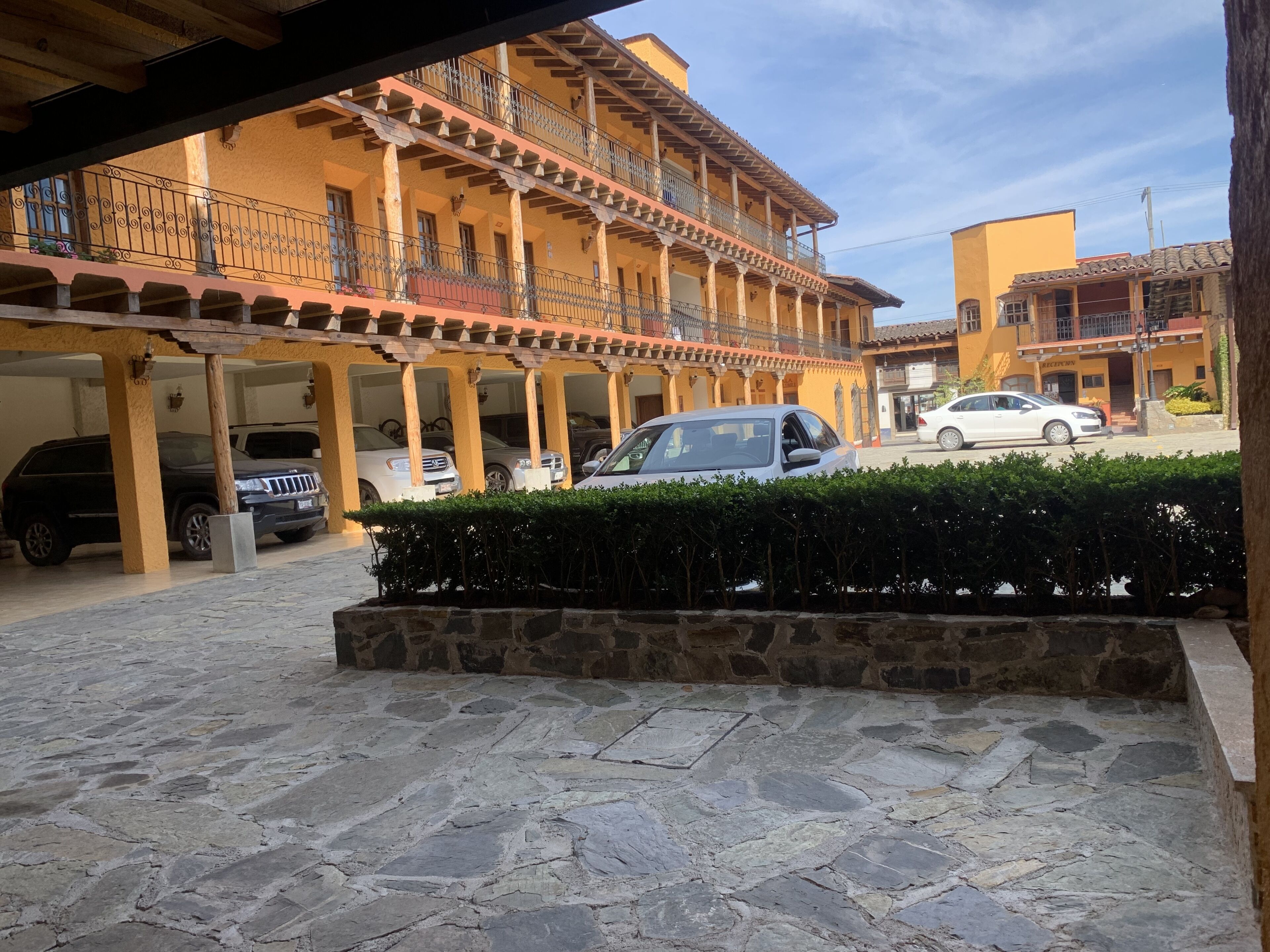 A courtyard with a stone floor, a covered area with columns, and a building with balconies.