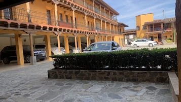 A courtyard with a stone floor, a covered area with columns, and a building with balconies.