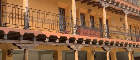 A multi-story building with balconies, wooden beams, and a row of parked cars.
