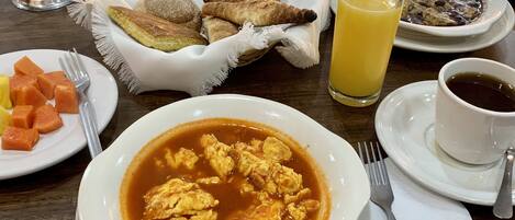 Una mesa con desayuno que incluye huevos revueltos, tostadas, fruta y un vaso de jugo de naranja.