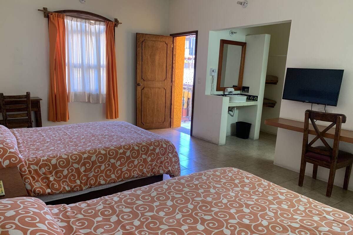 A hotel room with two beds, a desk, a chair, a TV, and a bathroom.
