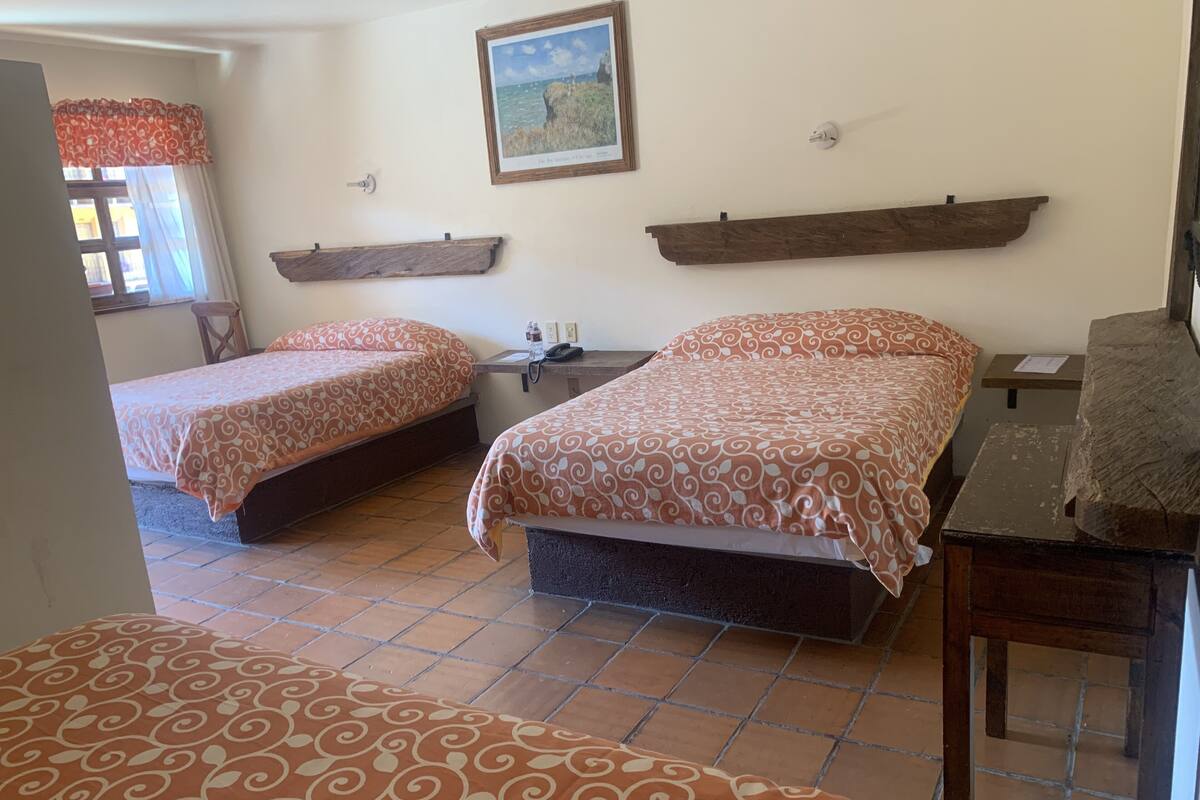 A room with two beds, a wooden shelf, a framed picture, and a tiled floor.