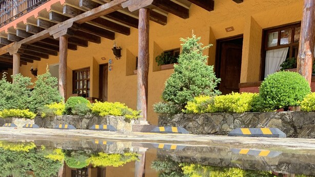 A hotel with a reflective pool, wooden balconies, and a stone wall with greenery.