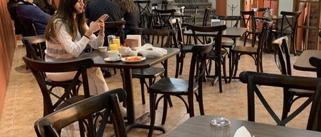 Un comedor con varias mesas y sillas, una escalera y vistas al exterior a través de amplios ventanales.