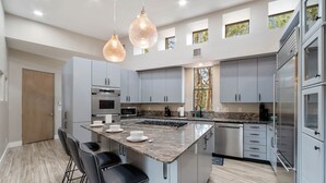 A modern kitchen with a central island, bar stools, and pendant lighting.