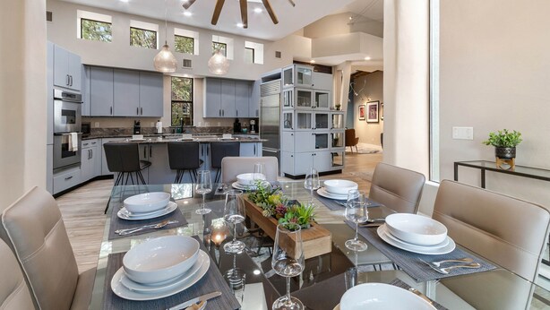 A modern kitchen with grey cabinets, a central island, and a dining area with a glass table set for six.