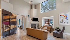 A spacious living room with a fireplace, leather sofas, and a large window offering a view of trees.