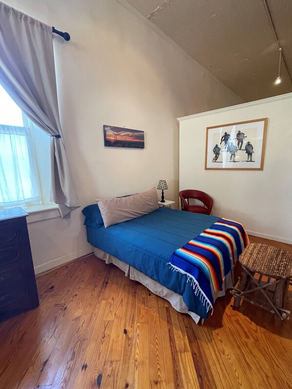A bedroom with a bed, a chair, a desk, a lamp, and artwork on the walls.