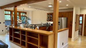 Una cocina amplia con armarios de madera, una isla central con estantes y un refrigerador de acero inoxidable.