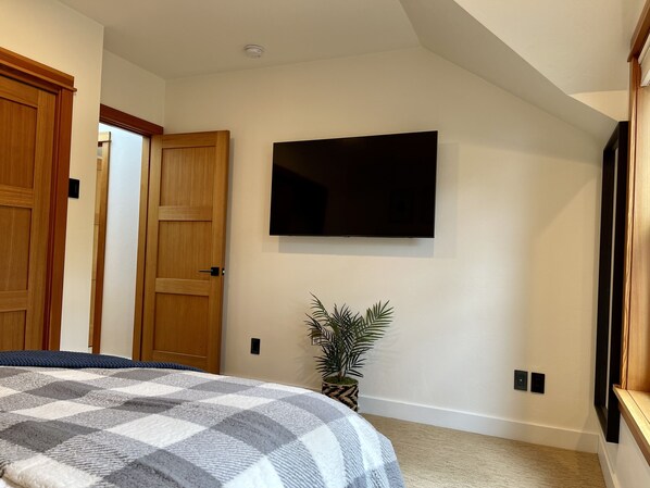 A bedroom with a large bed, a flat-screen TV mounted on the wall, a potted plant, and wooden doors. - Premier Eugene Craftsman + Private Wellness Yard, Hot Tub, Sauna and Walk to UO (Eugene)