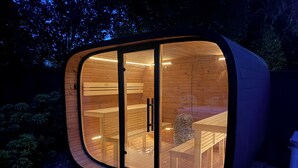 Una estructura moderna de madera curvada con puertas de vidrio, un banco y una mesa en el interior.