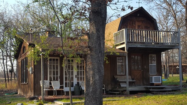 A rustic cabin with a porch, two chairs, and a large tree in front. - Cabin in the Woods - 10 minutes to Bartlesville (Bartlesville)