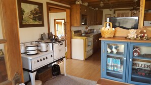 A kitchen with wooden cabinets, a stove, a refrigerator, and a small cabinet with books and a toy train. - Cabin in the Woods - 10 minutes to Bartlesville (Bartlesville)