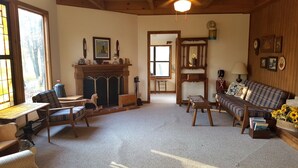 A cozy living room with a fireplace, wooden furniture, and a plaid sofa. - Cabin in the Woods - 10 minutes to Bartlesville (Bartlesville)