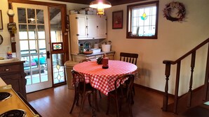 A dining area with a round table covered in a checkered tablecloth, wooden chairs, a kitchen in the background, and a staircase to the right. - Cabin in the Woods - 10 minutes to Bartlesville (Bartlesville)