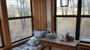 A cozy corner with a wooden bench, a small table, and a window with a view of trees. - Cabin in the Woods - 10 minutes to Bartlesville (Bartlesville)