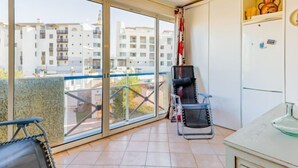 Uma varanda com vista para edifícios, uma cadeira, uma mesa e uma geladeira.