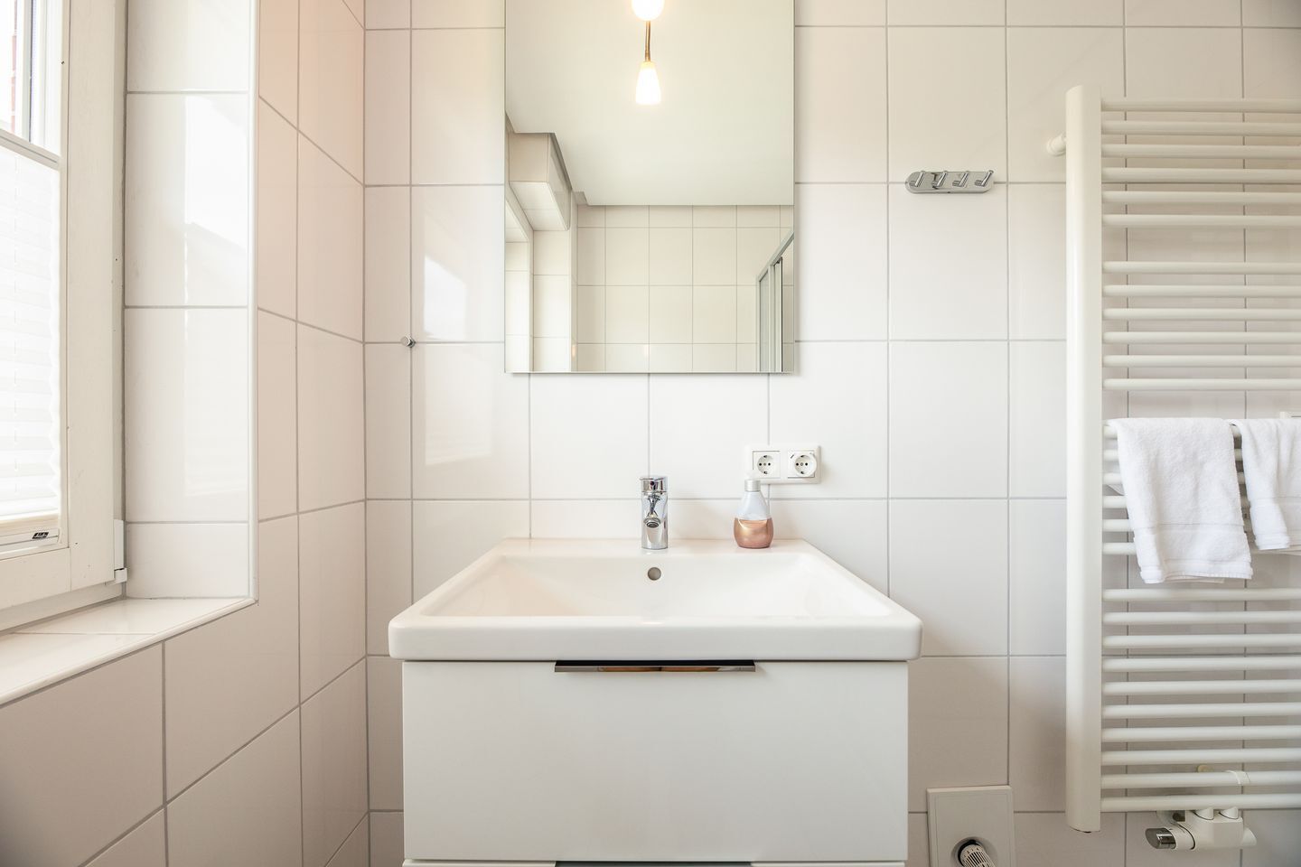 A modern bathroom with a white sink, a mirror, and a towel rack.