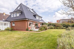 Ein zweistöckiges Haus mit Satteldach, Backsteinfassade und einer kleinen Veranda mit Sitzgelegenheit.