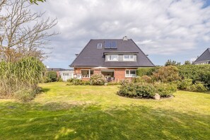 Ein zweistöckiges Haus mit geneigtem Dach, einer Veranda und einem kleinen Garten.