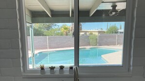 Une cuisine avec une fenêtre donnant sur une piscine, un évier et des plantes en pot sur le rebord de la fenêtre.