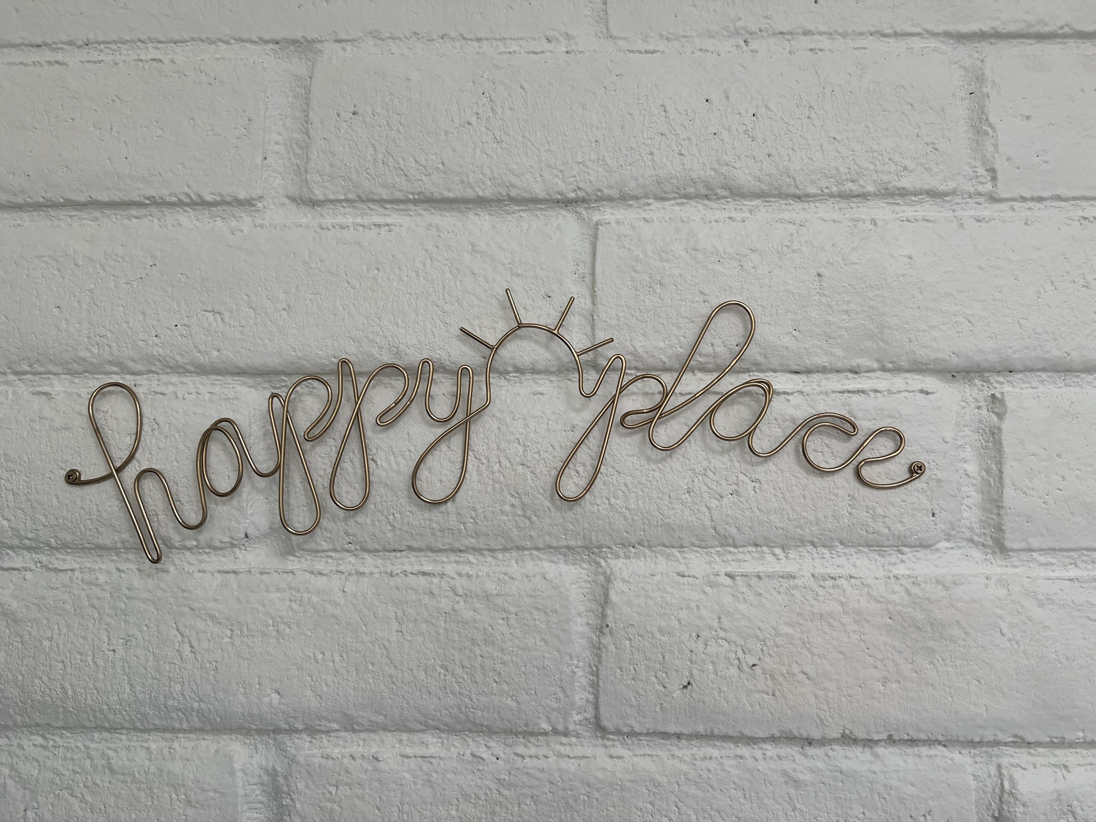 Un mur orné d’une pancarte en fil de fer sur laquelle est écrit « endroit où je suis heureux/se ».