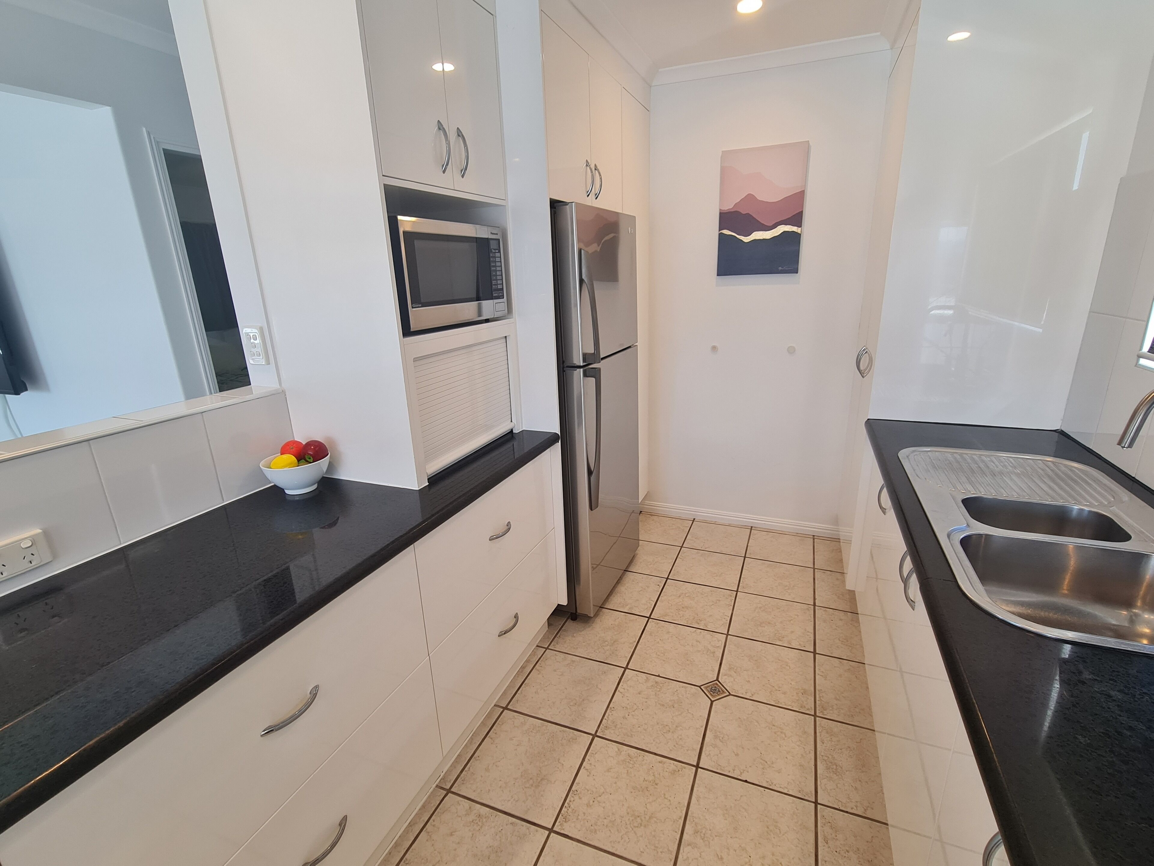 A modern kitchen with white cabinets, a stainless steel refrigerator, a microwave, and a sink.