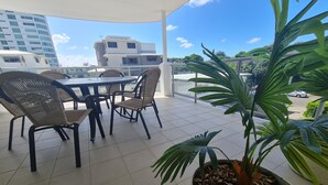 A covered outdoor seating area with wicker chairs and a table, surrounded by potted plants. - Cranbourne Court Beach Side Apartments (Maroochydore)