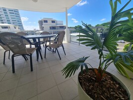 Un espace extérieur aménagé, abrité et doté de chaises en osier et d’une table, le tout entouré de plantes en pot.