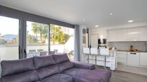 Una sala moderna con un sofá seccional, un comedor con sillas blancas y una cocina con gabinetes blancos.