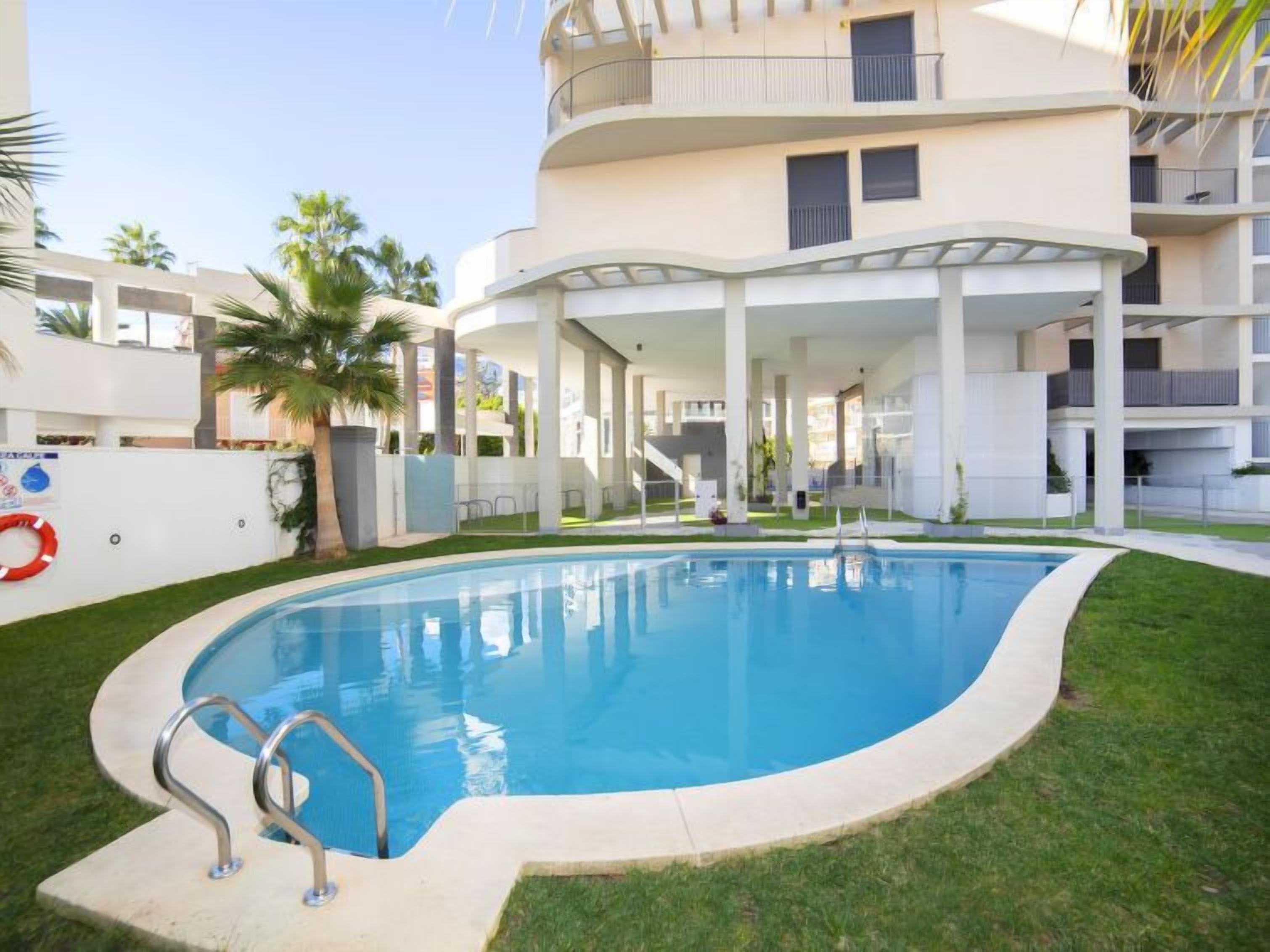 A modern building with a swimming pool surrounded by grass and palm trees.