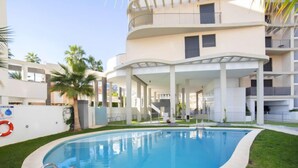 Un edificio moderno con piscina rodeada de césped y palmeras.