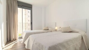 Habitación de hotel con dos camas, un ventanal grande con cortinas y un balcón.