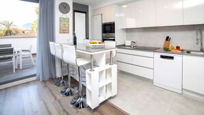 Una cocina moderna con armarios blancos, un lavamanos de acero inoxidable y una zona de comedor con sillas blancas.