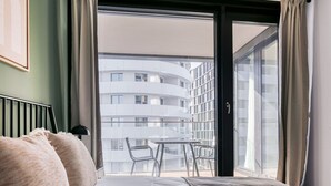 Un dormitorio con cama, mesita de noche, ventana con cortinas y vista a un edificio.