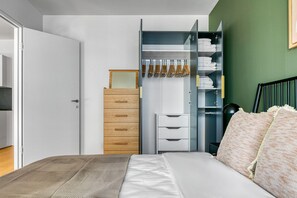 Ein Schlafzimmer mit einem Bett, einem Holzschrank, einem Kleiderschrank mit Kleidung und einem Nachttisch.