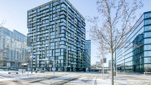 Un edificio moderno de gran altura con una fachada de ventanas y balcones, rodeado de otras construcciones contemporáneas.