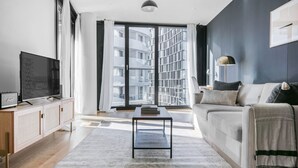 Una sala de estar moderna con sofá, una mesa de centro, televisor y un amplio ventanal con cortinas.