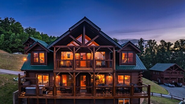 Une cabane en rondins à plusieurs étages, dotée d’un balcon, de grandes fenêtres et de fondations en pierre.