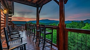 Une terrasse en bois, agrémentée de chaises et de tables, qui offre une vue sur un paysage montagneux.