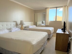 Two single beds with white linens, a TV and a mirror, set against a light-colored backdrop.