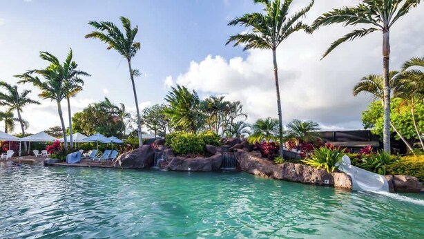 A pool area with clear water, palm trees, and lounge chairs. - 10 Bedroom Sleeps 24 w/ AC - Less than a 1 Minute Walk with views of Poipu Beach (Koloa)