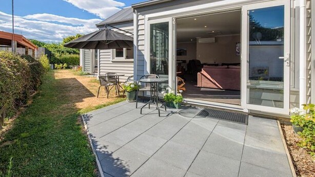 A patio area with a table and chairs, a sliding glass door leading to an interior space, and a small covered seating area. - Denbigh Escape - Perfect location, family-friendly! (Arrowtown)
