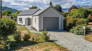 A single-story house with a garage, surrounded by a gravel driveway and small shrubs. - Denbigh Escape - Perfect location, family-friendly! (Arrowtown)