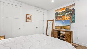 Een slaapkamer met een groot bed, een houten tv-meubel en een schilderij aan de muur.