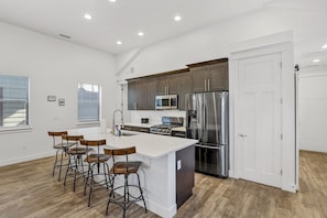 A modern kitchen with a large island, stainless steel appliances, and wooden bar stools.