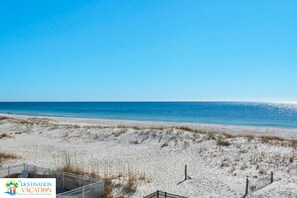 A beach with a clear sky, sandy shore, and a fenced area with a structure that could be a beach hut or a small building.